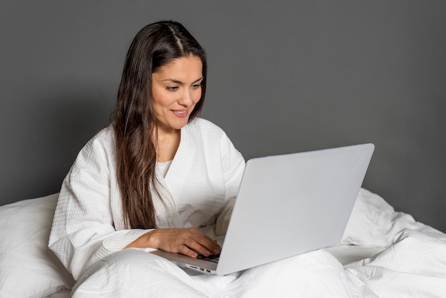 Donna dell'angolo alto a letto con il computer portatile
