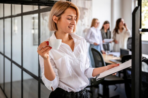 Donna dell'angolo alto che controlla i piani e che beve caffè