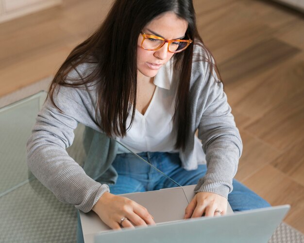 Donna dell'angolo alto che lavora al computer portatile che si siede sul pavimento