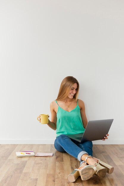 Donna dell'angolo alto sul pavimento che lavora al computer portatile