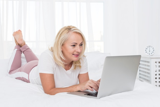Donna della foto a figura intera con il computer portatile a letto