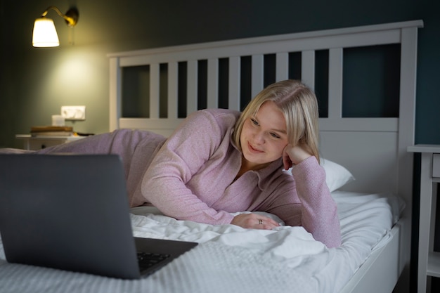 Donna della foto a figura intera con il computer portatile a letto