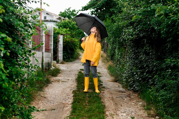Donna della possibilità remota in vestiti di pioggia che tengono un ombrello