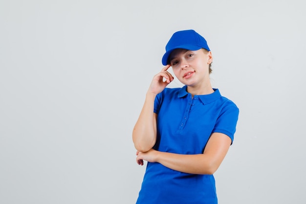 Donna delle consegne in maglietta blu e cappuccio che si appoggia alle tempie sul dito e sembra speranzosa