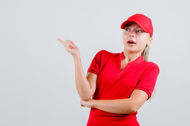 Donna delle consegne in maglietta rossa e berretto che punta lontano e sembra stupita
