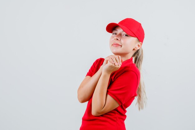 Donna delle consegne in maglietta rossa e berretto tenendo le mani giunte e guardando allegra