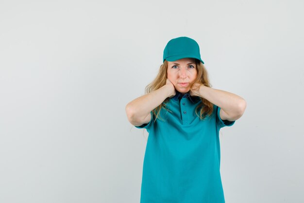 Donna delle consegne in t-shirt, berretto tenendo le mani sul collo e guardando pensieroso