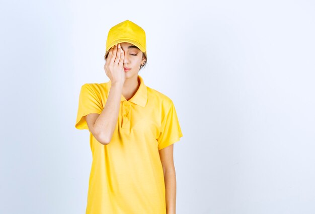 Donna delle consegne in uniforme gialla in piedi con la faccia assonnata e gli occhi chiusi.