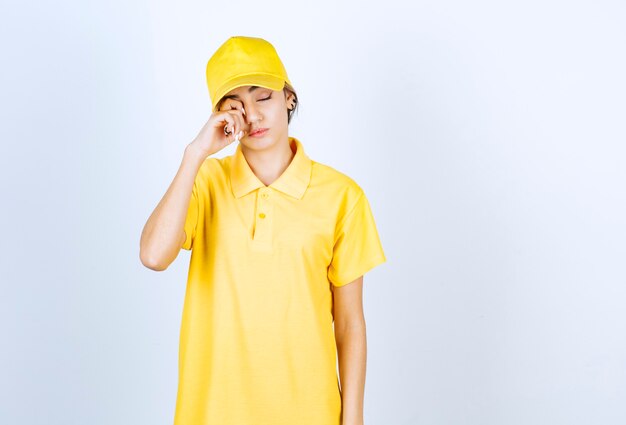 Donna delle consegne in uniforme gialla in piedi con la faccia assonnata e gli occhi chiusi.