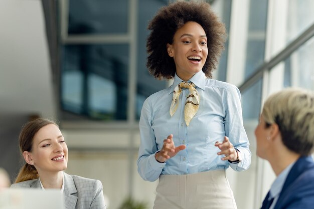 Donna di affari afroamericana felice che parla con le colleghe in ufficio