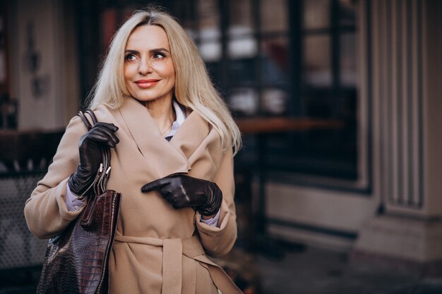 Donna di affari anziana in un cappotto che indossa i guanti in strada