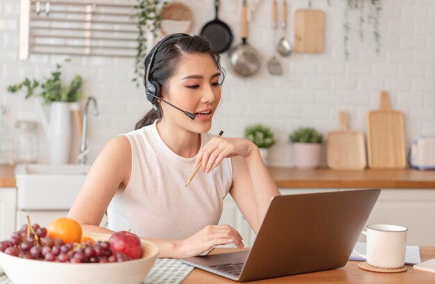 Donna di affari asiatica che usa il computer portatile che parla per il lavoro di riunione di videochiamata da casa