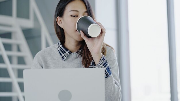 Donna di affari asiatica professionale che lavora al suo ufficio tramite computer portatile.