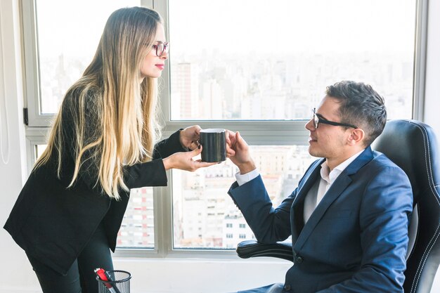 Donna di affari che dà caffè al suo capo nell&#39;ufficio