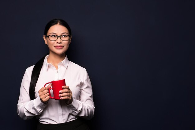 Donna di affari che gode della pausa caffè che tiene tazza rossa isolata su fondo scuro