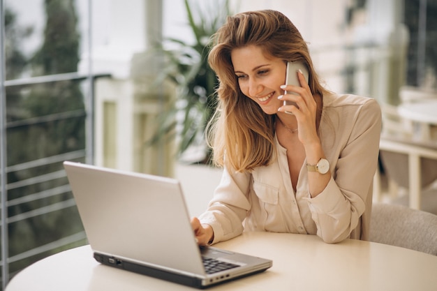 Donna di affari che lavora al computer portatile e parlando al telefono