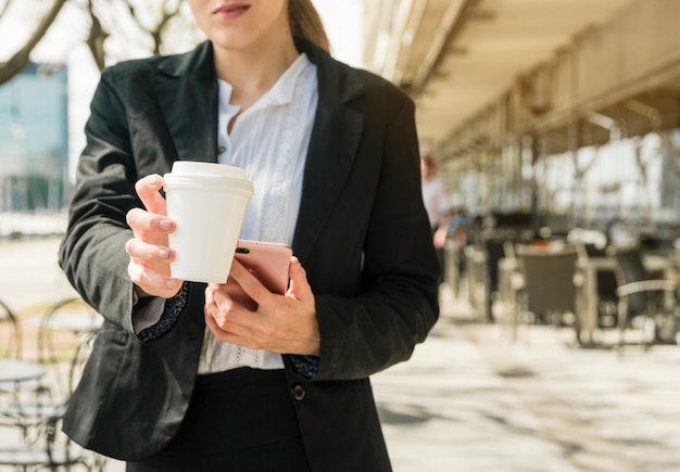 Donna di affari che passa la tazza di caffè asportabile che sta nel ristorante all&#39;aperto