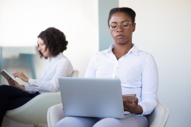 Donna di affari che per mezzo del computer portatile e dello smartphone