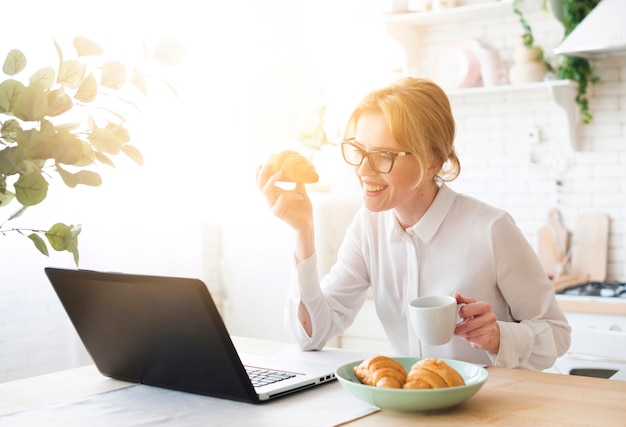 Donna di affari che per mezzo del computer portatile mentre mangiando croissant