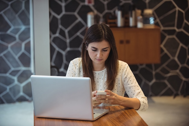 Donna di affari che per mezzo del telefono cellulare con il computer portatile sulla tavola