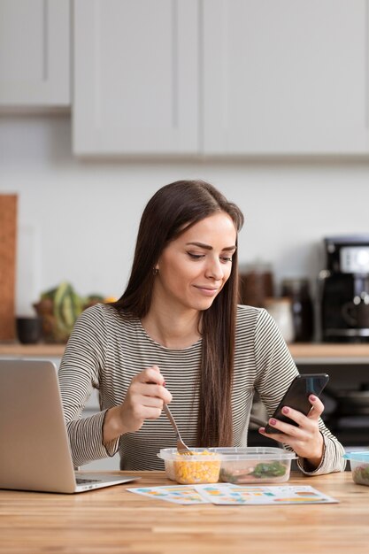 Donna di affari che prova a mangiare e lavorare dal suo telefono