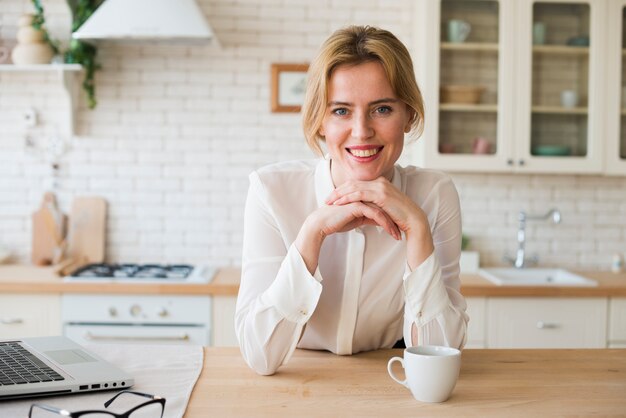 Donna di affari che si siede con la tazza e il computer portatile di caffè