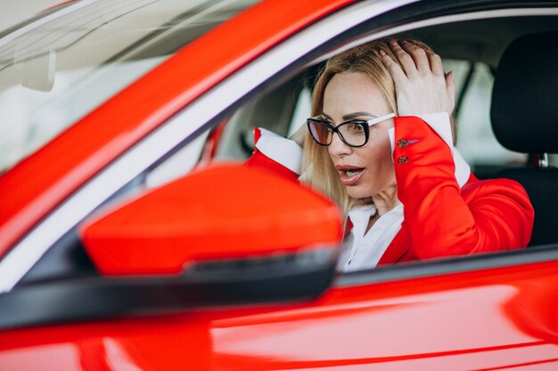 Donna di affari che si siede in una nuova automobile in una sala d'esposizione dell'automobile