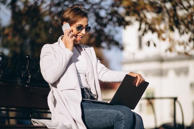 Donna di affari che si siede su una panchina con telefono bere caffè