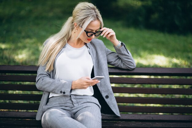 Donna di affari che si siede sul banco in sosta che comunica sul telefono