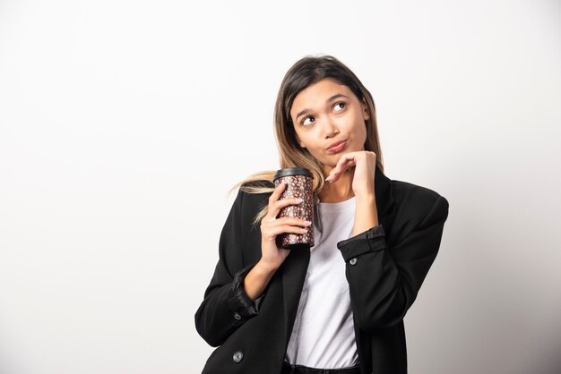 Donna di affari che tiene tazza e posa sul muro bianco.