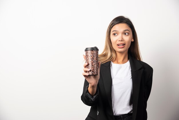 Donna di affari che tiene tazza e posa sul muro bianco.