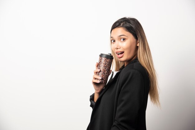 Donna di affari che tiene tazza e posa sul muro bianco.