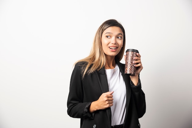 Donna di affari che tiene tazza e posa sul muro bianco.