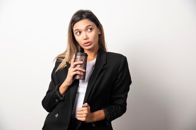 Donna di affari che tiene tazza e posa sul muro bianco.