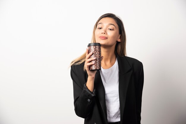 Donna di affari che tiene tazza e posa sul muro bianco.