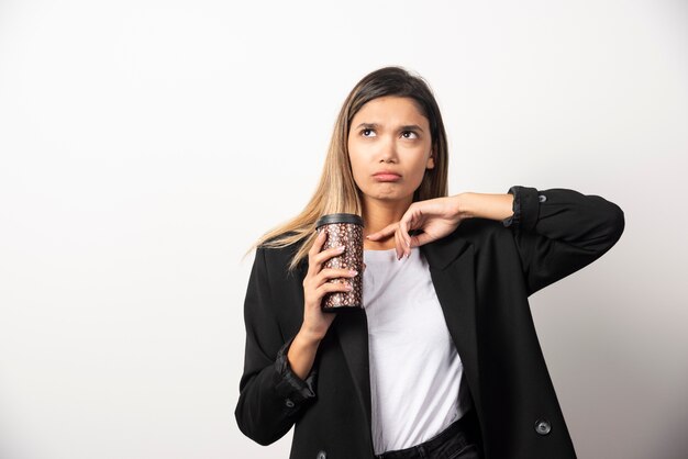 Donna di affari che tiene tazza e posa sul muro bianco.