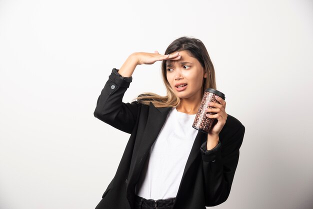 Donna di affari che tiene tazza e posa sul muro bianco.