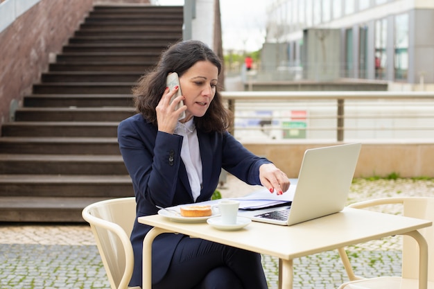 Donna di affari che utilizza computer portatile e smartphone nel caffè