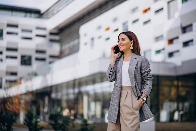 Donna di affari che utilizza telefono fuori nella via dall&#39;edificio