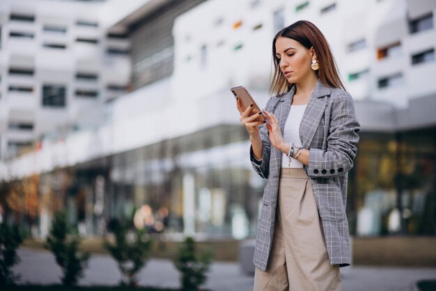 Donna di affari che utilizza telefono fuori nella via dall&#39;edificio