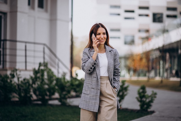 Donna di affari che utilizza telefono fuori nella via dall&#39;edificio