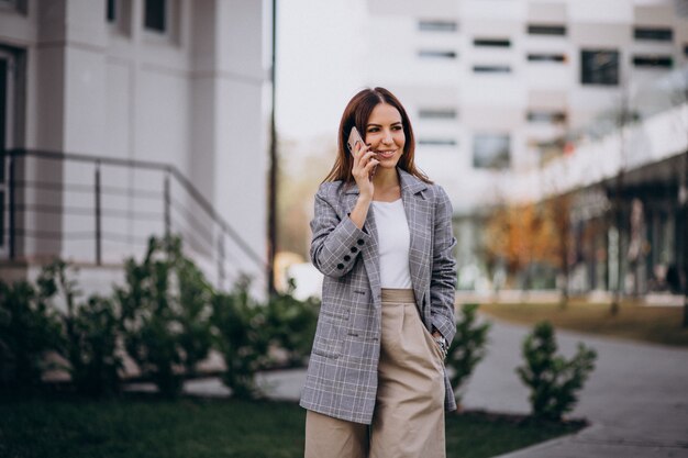 Donna di affari che utilizza telefono fuori nella via dall&#39;edificio