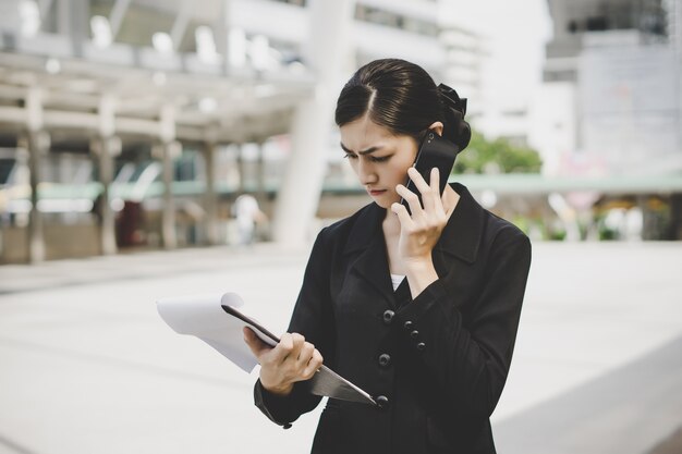 Donna di affari con documento a disposizione che parla sul telefono cellulare vicino al centro di affari