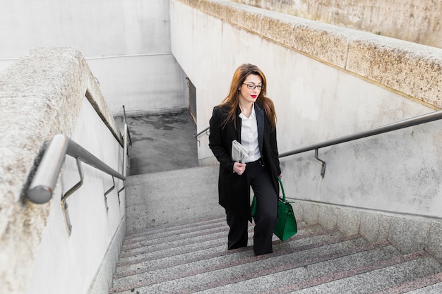 Donna di affari con il giornale e borsa che cammina sulle scale