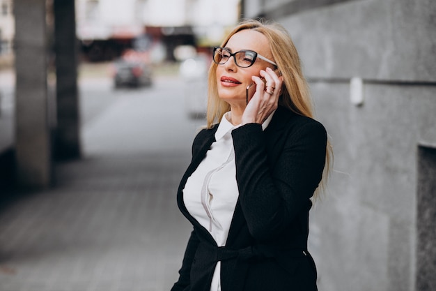 Donna di affari di mezza età che per mezzo del telefono fuori del centro di affari