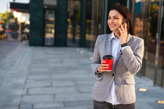 Donna di affari di smiley che parla sul telefono mentre beve caffè con lo spazio della copia