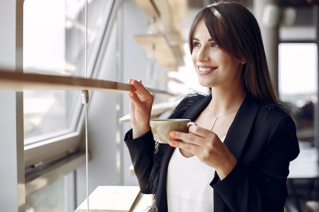 Donna di affari elegante che lavora in un ufficio e che beve un caffè