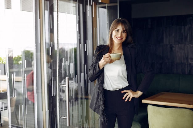 Donna di affari elegante che lavora in un ufficio e che beve un caffè