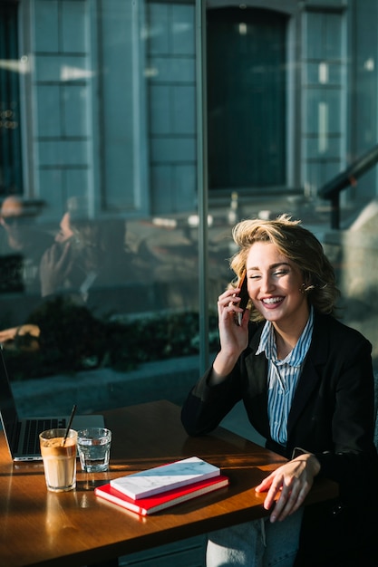 Donna di affari felice che si siede nel ristorante facendo uso del telefono cellulare