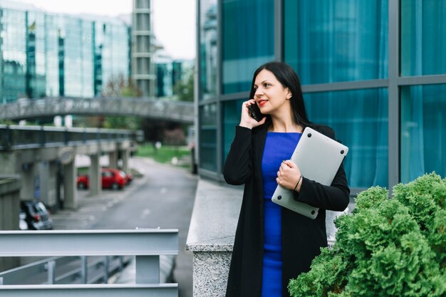 Donna di affari felice con il computer portatile che parla sullo smartphone